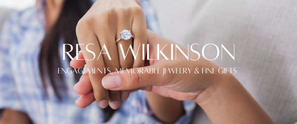 A close-up of a person's hand wearing a diamond engagement ring, with another hand holding it. Large white text across the center reads 'RESA WILKINSON' with smaller text below reading 'ENGAGEMENTS, MEMORABLE JEWELRY & FINE GIFTS'.